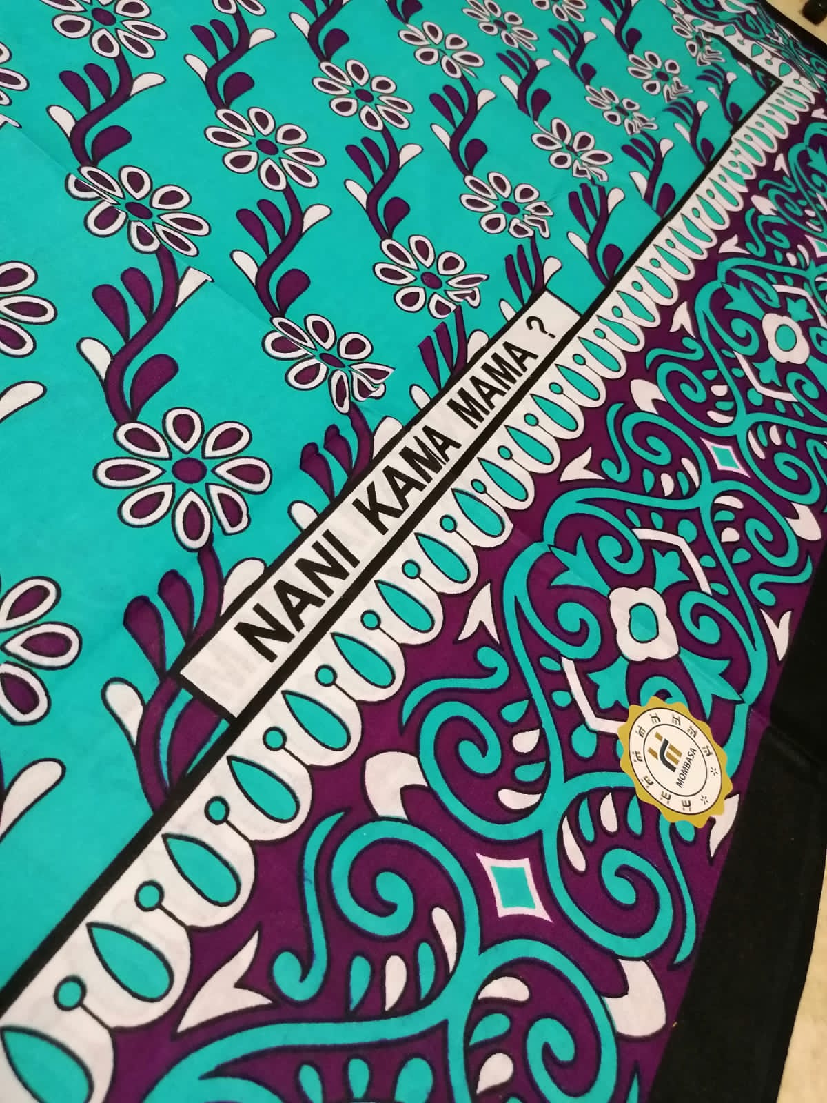 Kanga Mombasa, modrá s květy, text "Kdo je jako máma?"